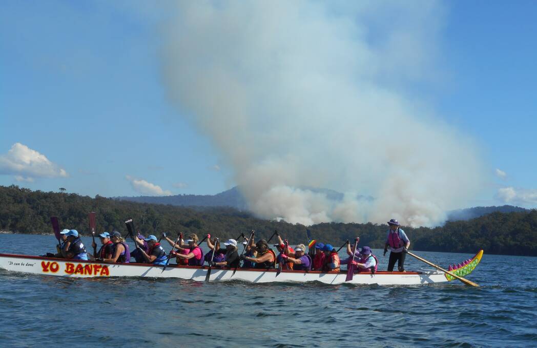 Paddling past the plume: One of the dragon boats near Mallacoota with hazard reduction burn in the background.