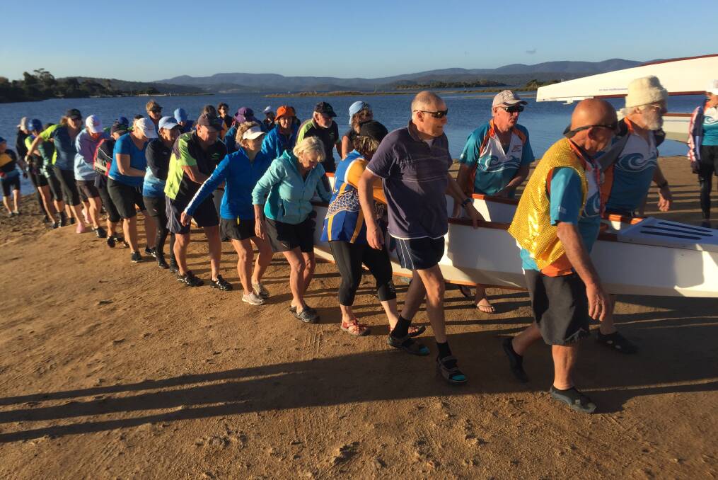 READY, STEADY, LIFT: Dragon boat paddlers bringing one of the boats ashore at Mallacoota after the paddle from Gipsy Point.
