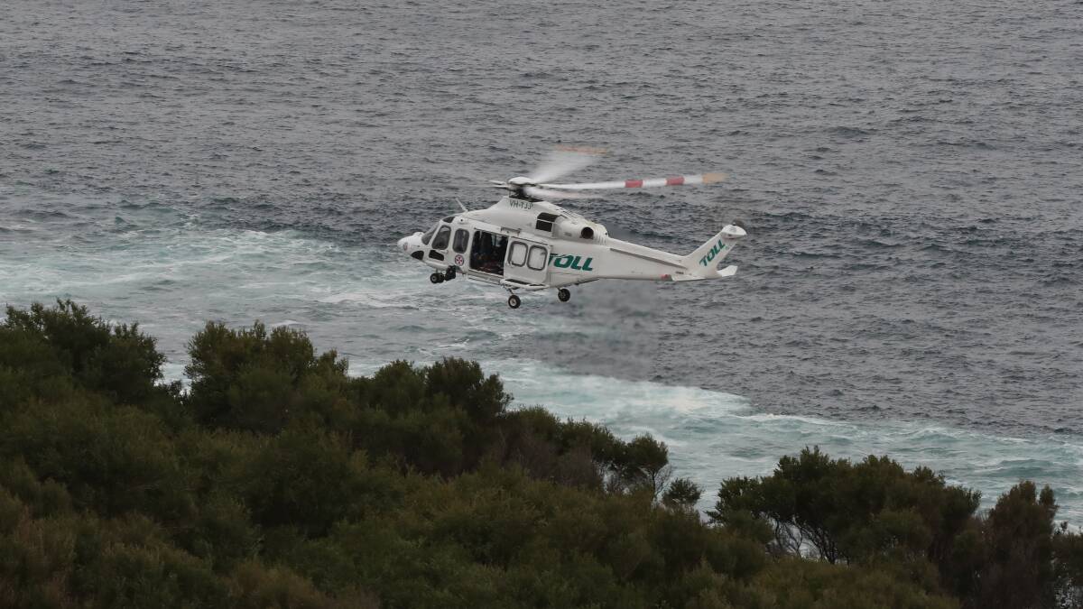 The Toll rescue helicopter hovers off Port Kembla on Monday, during the search for a missing 19-year-old swept off rocks. Picture: Robert Peet