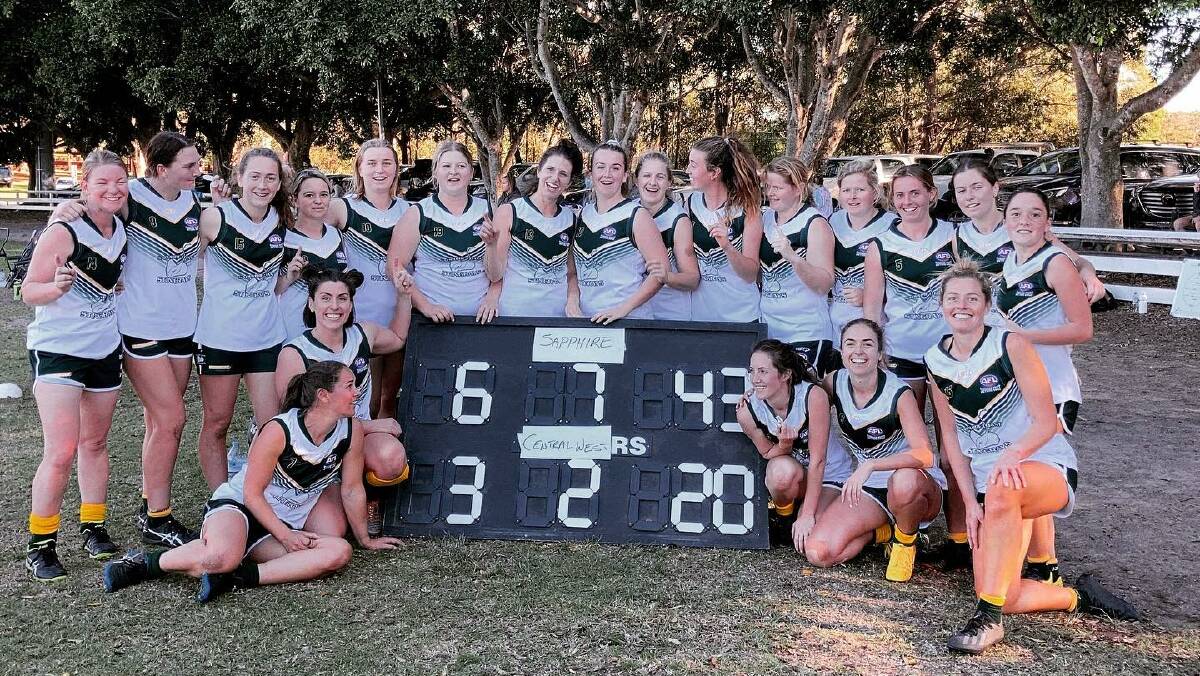 The Sapphire Coast Stingrays women's squad stop for a team photo with the scoreboard from their win over the weekend. 